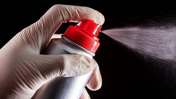 Gloved hand spraying a fine mist of WD-40